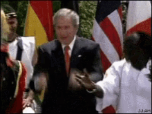 a man in a suit and tie is shaking hands with a man in a white shirt in front of flags