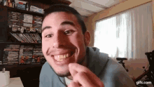 a man with a beard is smiling while holding a piece of food in front of a bookshelf filled with dvds .