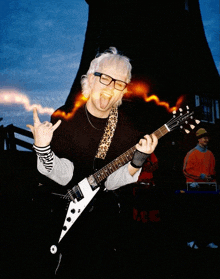 a man wearing glasses is playing a guitar and making a horn sign