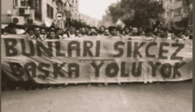 a black and white photo of a group of people holding a banner that says bunlari sikcez baska yolu yok