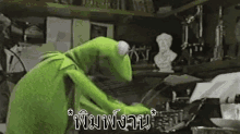 kermit the frog is using a typewriter in a room with a statue in the background .