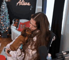 a woman is holding a small brown dog in her lap with a sign that says allison on the wall behind her