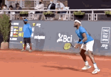 a man in a blue shirt is playing tennis on a court with a bci logo on the wall behind him