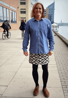 a woman wearing a denim shirt and a skirt stands on a sidewalk