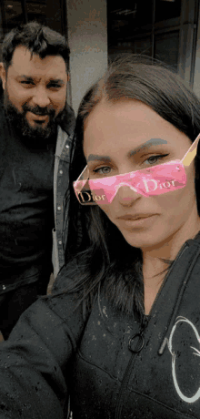 a woman wearing a pair of pink dior sunglasses stands next to a man