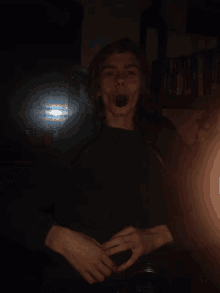 a young man is making a funny face in a dark room with bookshelves in the background