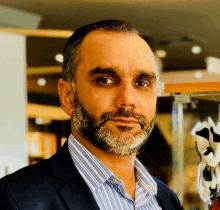 a man with a beard wearing a suit and striped shirt looks at the camera