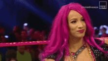 a woman with pink hair is standing in a wrestling ring and smiling .