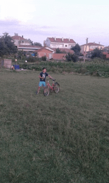 a young boy riding a bicycle in a grassy field with houses in the background