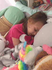 a little girl laying on a bed with stuffed animals including a stuffed unicorn