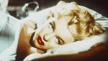 a woman with red lipstick is laying on a pillow