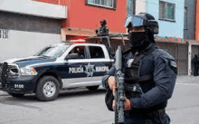 a mexican police officer is holding a gun in front of a police car .