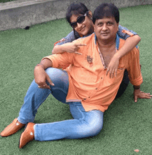 a man in an orange shirt is laying on the grass with his arm around a woman