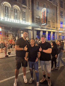 three men are posing for a picture in front of a building that says lucky bastard saloon