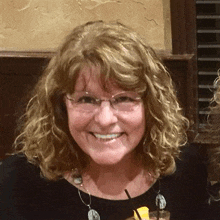 a woman wearing glasses and a necklace is smiling and holding a drink with a straw .