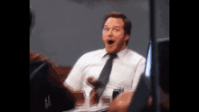 a man in a white shirt and tie is sitting at a table with his mouth open