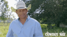 a man wearing a cowboy hat and a blue shirt is standing in a field with the cowboy way written on the bottom