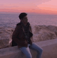 a young man is sitting on a wall overlooking the ocean .