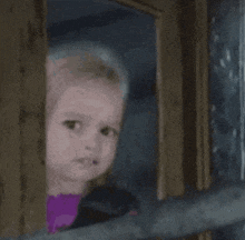 a little girl is looking out of a window with a sad look on her face .