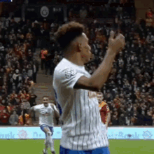 a man in a white and blue striped shirt is standing on a soccer field with his fist in the air .