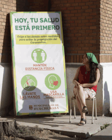 a woman sits in a chair in front of a sign that says hoy tu salud esta primero