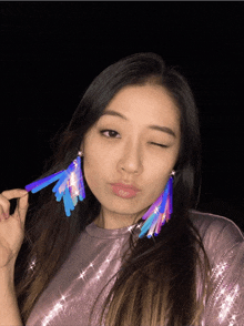 a woman wearing a purple top and a pair of earrings winks at the camera