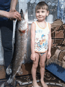 a little boy is standing next to a large fish in a living room .