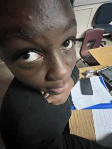 a young boy sitting at a desk with a cell phone on the desk