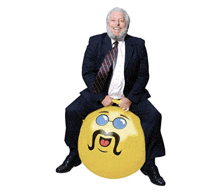 a man in a suit and tie is sitting on a yellow bouncy ball with a face on it