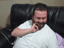 a man with a beard is sitting on a black leather couch and smiling