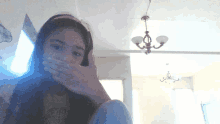 a girl covering her mouth with her hand in a room with a chandelier