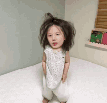 a little girl with a messy hairdo is standing on a bed