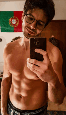 a shirtless man taking a selfie in front of a flag that says portugal