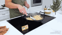 a man is stirring noodles in a wok on a stove top with a box of ranch dressing in the background