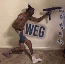 a shirtless man is holding a gun in front of a wall that has weg written on it