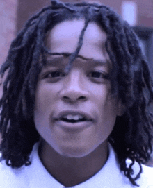 a young man with dreadlocks and a white shirt is smiling