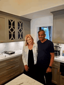 a man and a woman stand in a kitchen smiling