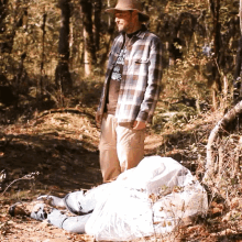 a man wearing a plaid shirt that says ' i 'm a cowboy ' on it stands in the woods