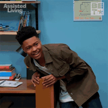 a young man in a military jacket is standing next to a desk with a sign that says assisted living on it