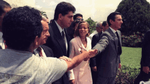 a man shakes hands with a woman in a pink suit and a man in a black suit