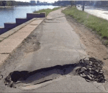 a hole in the side of a road next to a body of water