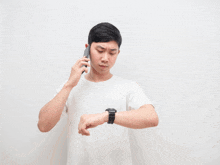 a man in a white shirt is talking on a cell phone and looking at his watch