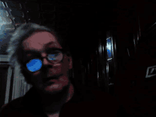 a man wearing glasses looks at the camera in a dark hallway