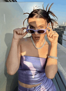 a woman wearing sunglasses and a purple top is standing on a balcony