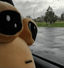 a stuffed animal is sitting in a car looking out the window on a rainy day .