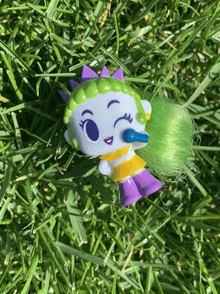 a toy with green hair and purple ears is sitting in the grass