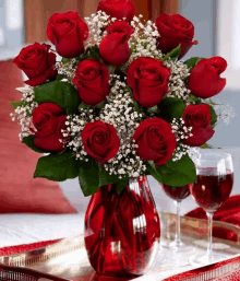 a vase filled with red roses and baby 's breath sits on a table next to two glasses of wine