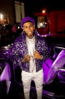 a man wearing a purple jacket and a purple bandana is standing next to a purple car .