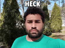 a man in a green shirt is standing in front of trees with the word heck above him