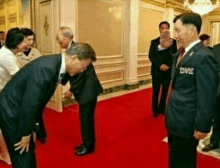 a man in a suit and tie is bowing to another man